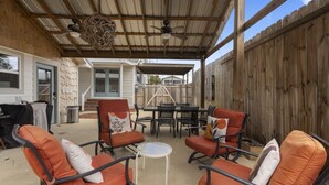 An outdoor patio with orange chairs and a table, a ceiling fan, and a wooden fence.