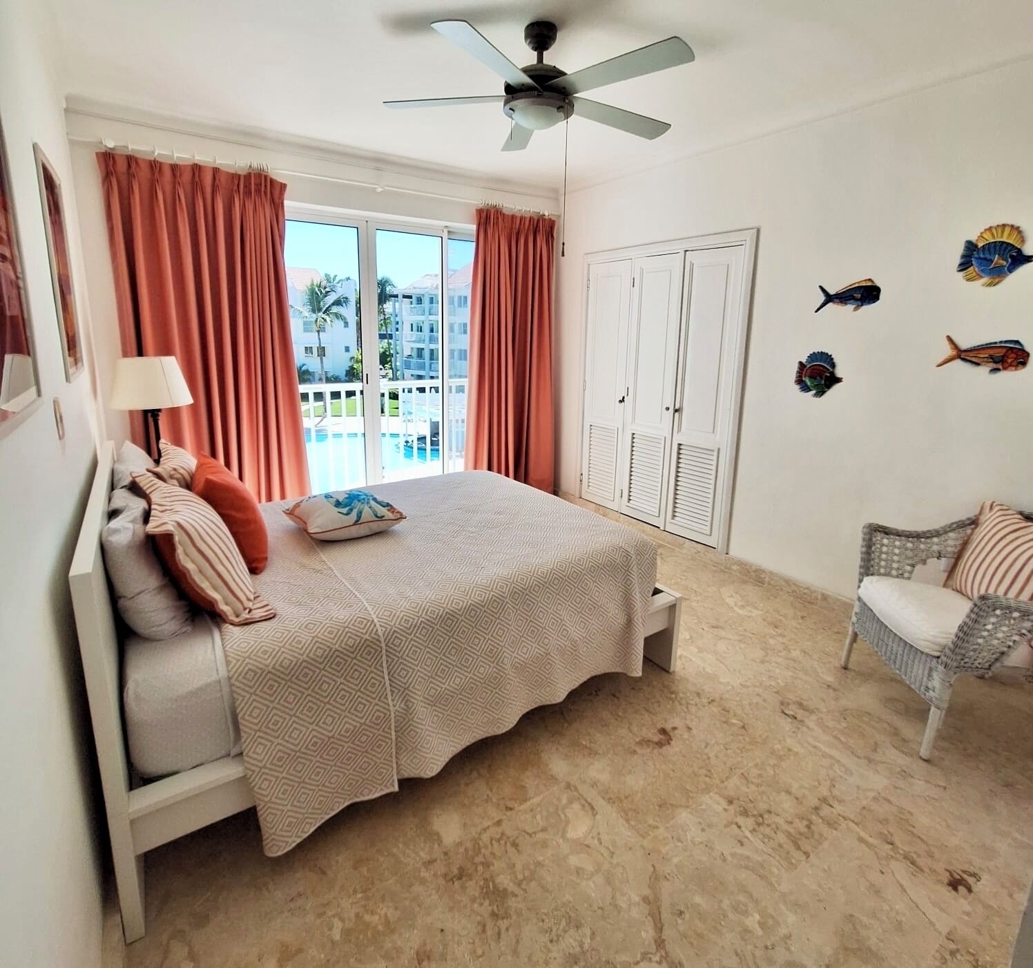 Ein Schlafzimmer mit einem Bett, einem Sessel, einem Deckenventilator und Blick auf einen Pool sowie Gebäude.
