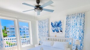 Un dormitorio con una cama grande, ventilador de techo, vistas a la ciudad y un balcón con cortinas.