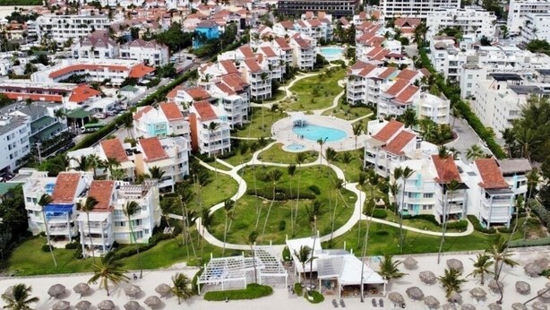 Un resort con varias construcciones, una piscina central y una zona de playa con sombrillas.