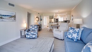 Un salón espacioso con un sofá azul, un sillón estampado y un comedor al fondo.