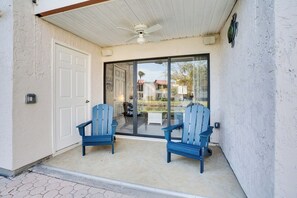 A covered patio with two blue chairs, a ceiling fan, and a sliding glass door leading to a pool area.
