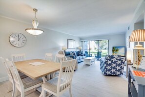 En moderne stue med spisebord, hvide stole, en blå sofa og en mønstret skammel.