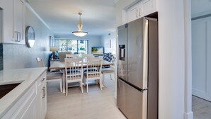 Una cocina moderna con armarios blancos, un refrigerador de acero inoxidable y un comedor con mesa de madera y sillas blancas.