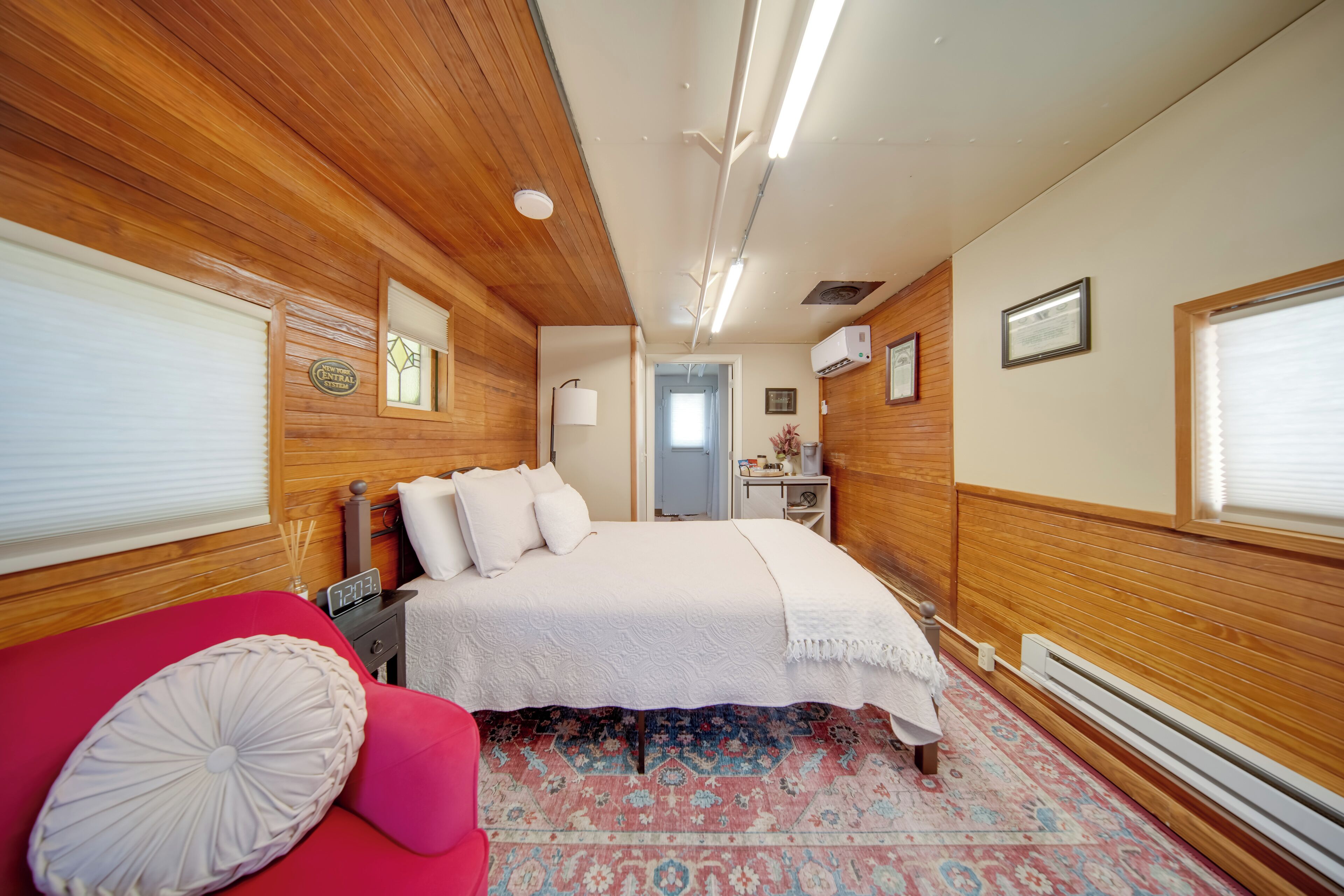 Un dormitorio con techo de madera, una cama con ropa de cama blanca, una silla roja y una alfombra estampada.
