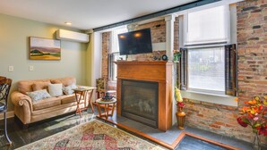 A living room with a fireplace, a sofa, a TV mounted on the wall, and a brick wall.
