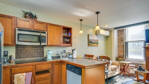 A kitchen with wooden cabinets, a built-in microwave, and a dishwasher. There is a dining area with a table and chairs, and a window with a view of the outdoors.