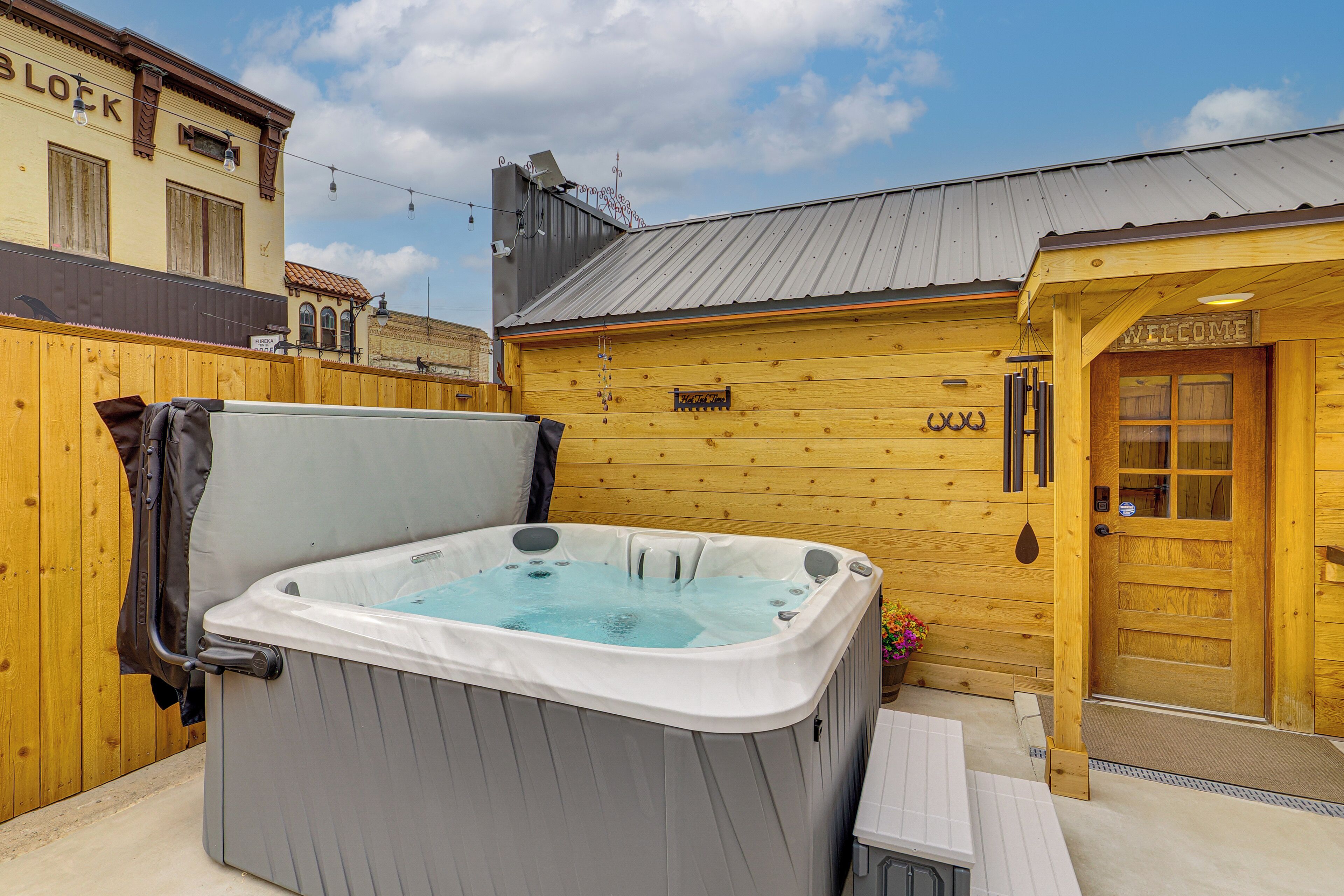 Un bâtiment en bois avec une porte en bois sur laquelle est écrit « BIENVENUE » et un jacuzzi à l’avant.