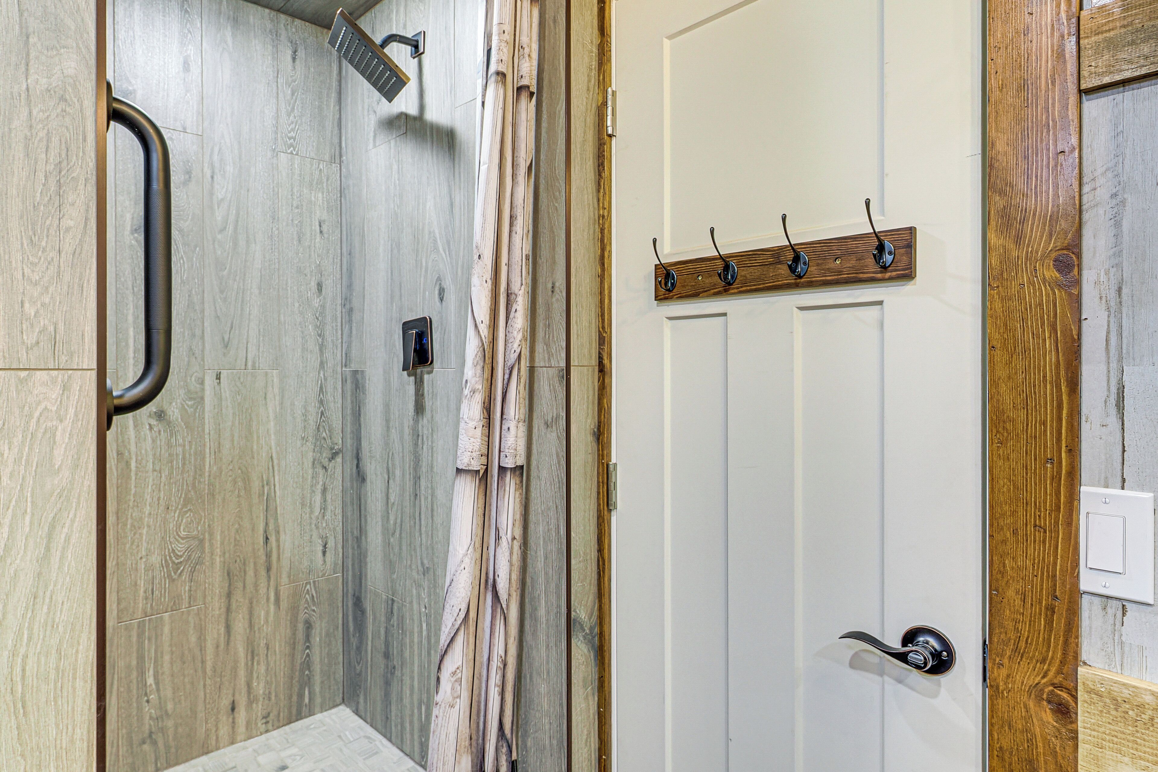 A bathroom with a shower, a white door with a wooden frame, and a towel rack.