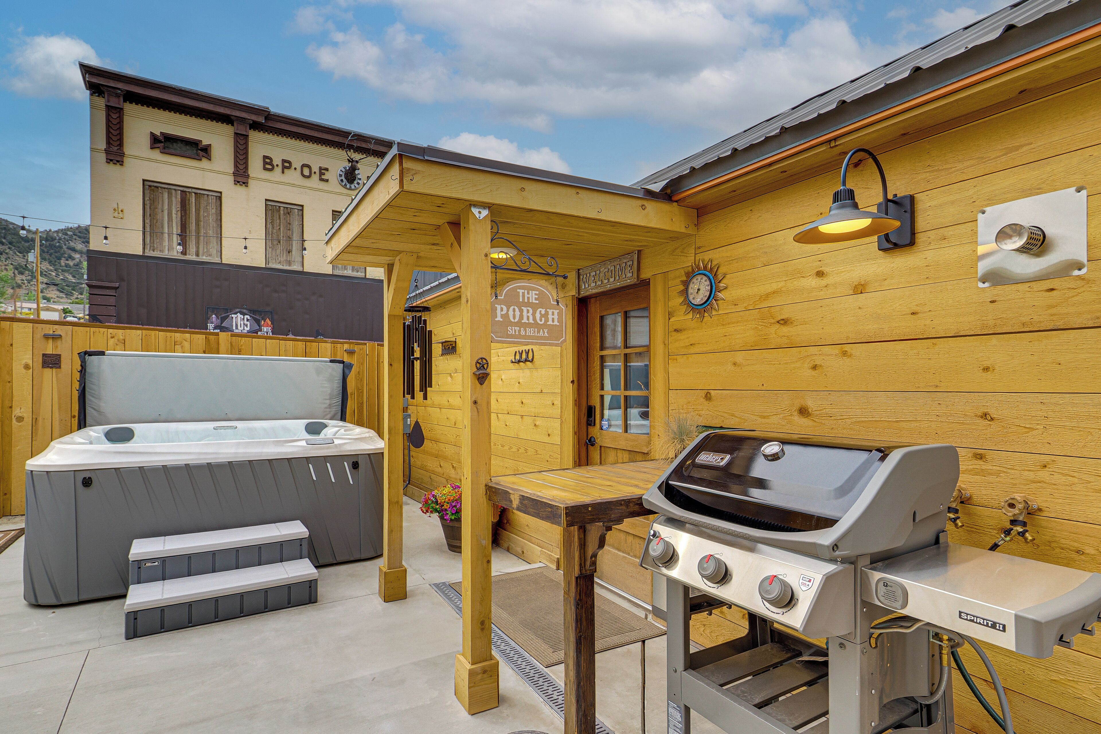 Une construction en bois dotée d’un bain à remous, d’un barbecue et d’une pancarte sur laquelle on peut lire : « Le Porche : asseyez-vous et détendez-vous ».