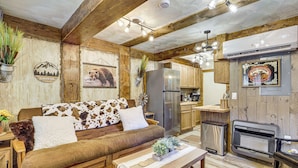 Interior rústico de una cabaña con sofá de madera, una mesa de comedor, zona de cocina y chimenea.