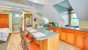 A kitchen with a central island, wooden cabinets, and a dining area with a table and chairs. - Walk to Marina: Dog-friendly Lake Ontario Studio (Sackets Harbor)