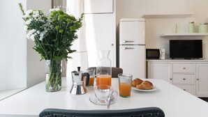 Una mesa de desayuno con un jarrón de flores, una cafetera, una jarra, vasos de jugo de naranja y croissants.