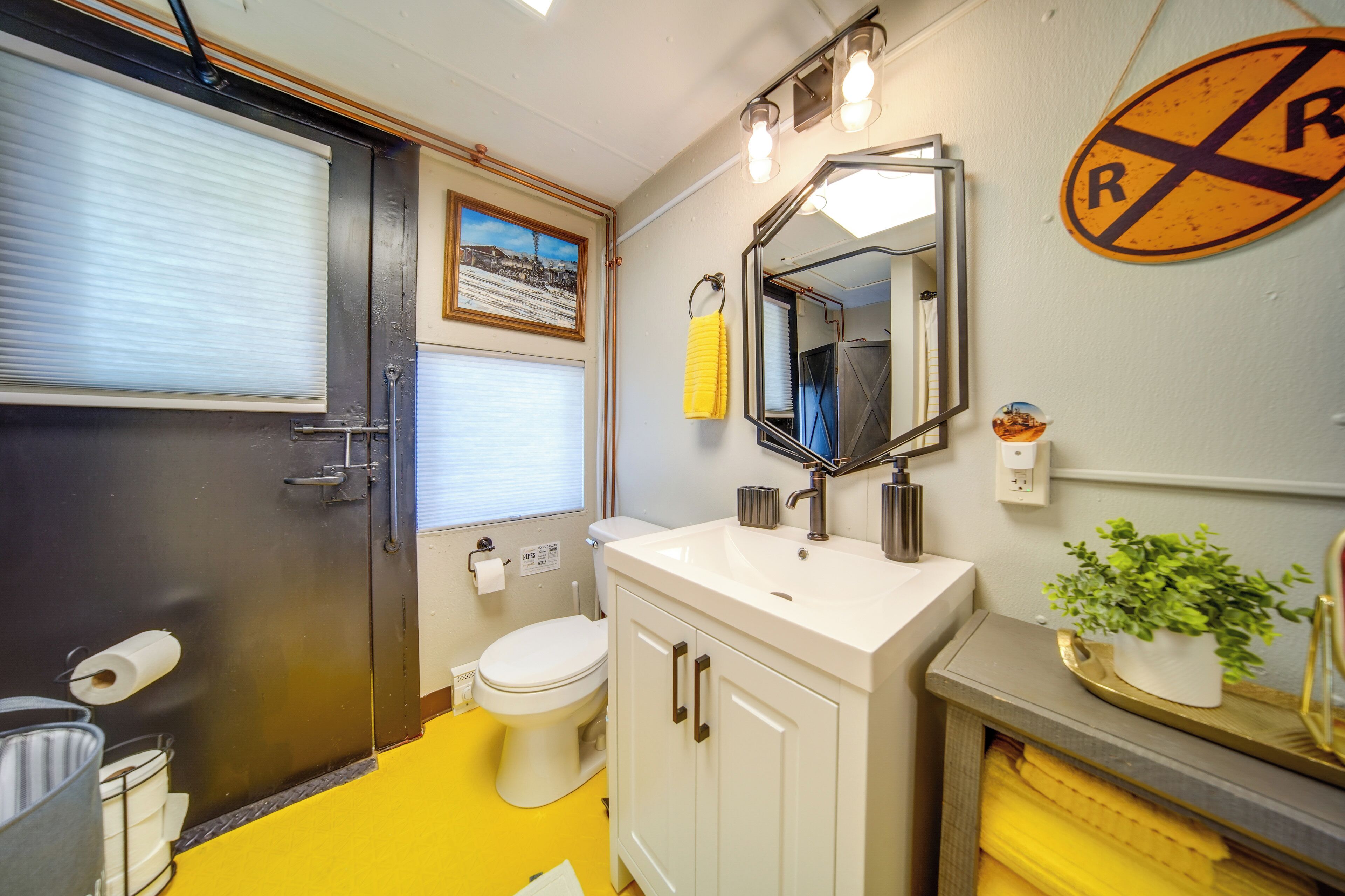Een badkamer met toilet, wastafel, spiegel en een gele handdoek aan de muur.