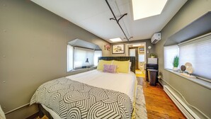 Un dormitorio con una cama grande, una ventana con persianas, un ventilador de techo y una pequeña mesa con una planta.