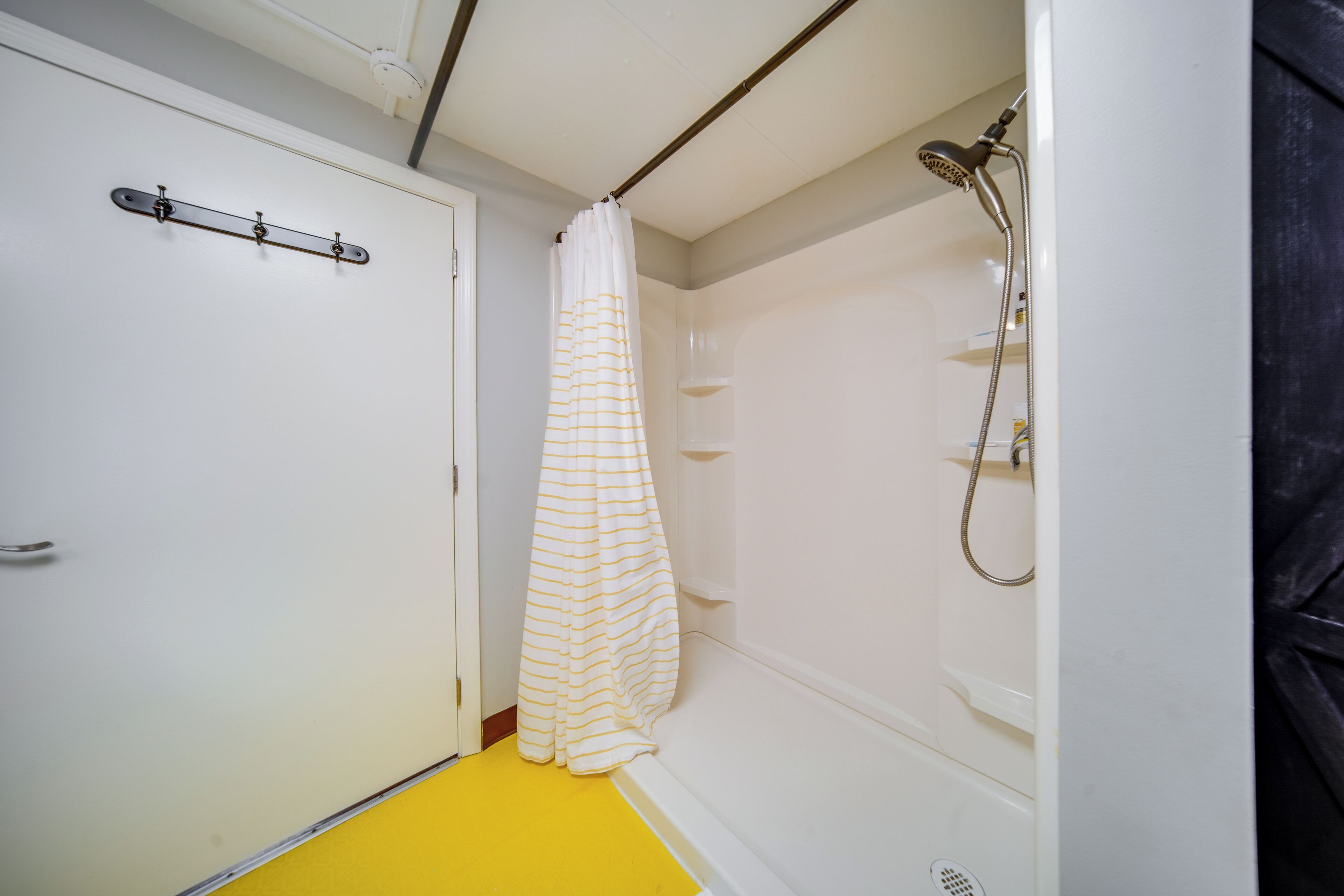 Un bagno con doccia, pavimento giallo e porta bianca.