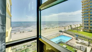 A view from a hotel room overlooking a beach, a swimming pool, and a high-rise building. - Beachfront Studio: Walk to Daytona Fun! (Daytona Beach Shores)