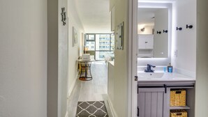 A hallway leading to a bathroom with a sink, mirror, and storage baskets. - Beachfront Studio: Walk to Daytona Fun! (Daytona Beach Shores)