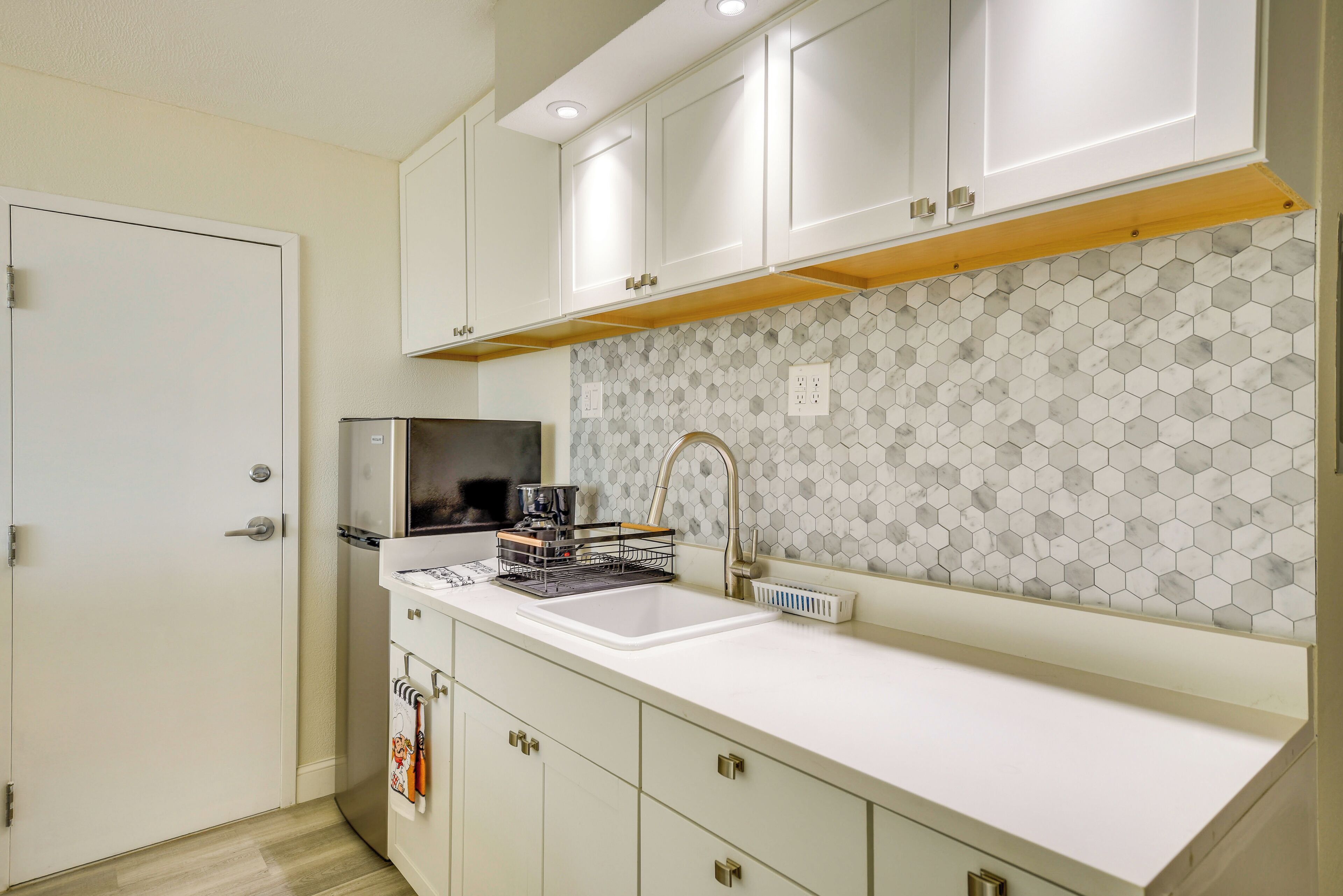 Una cocina con armarios blancos, encimera blanca, salpicadero de azulejos hexagonales y horno empotrado.
