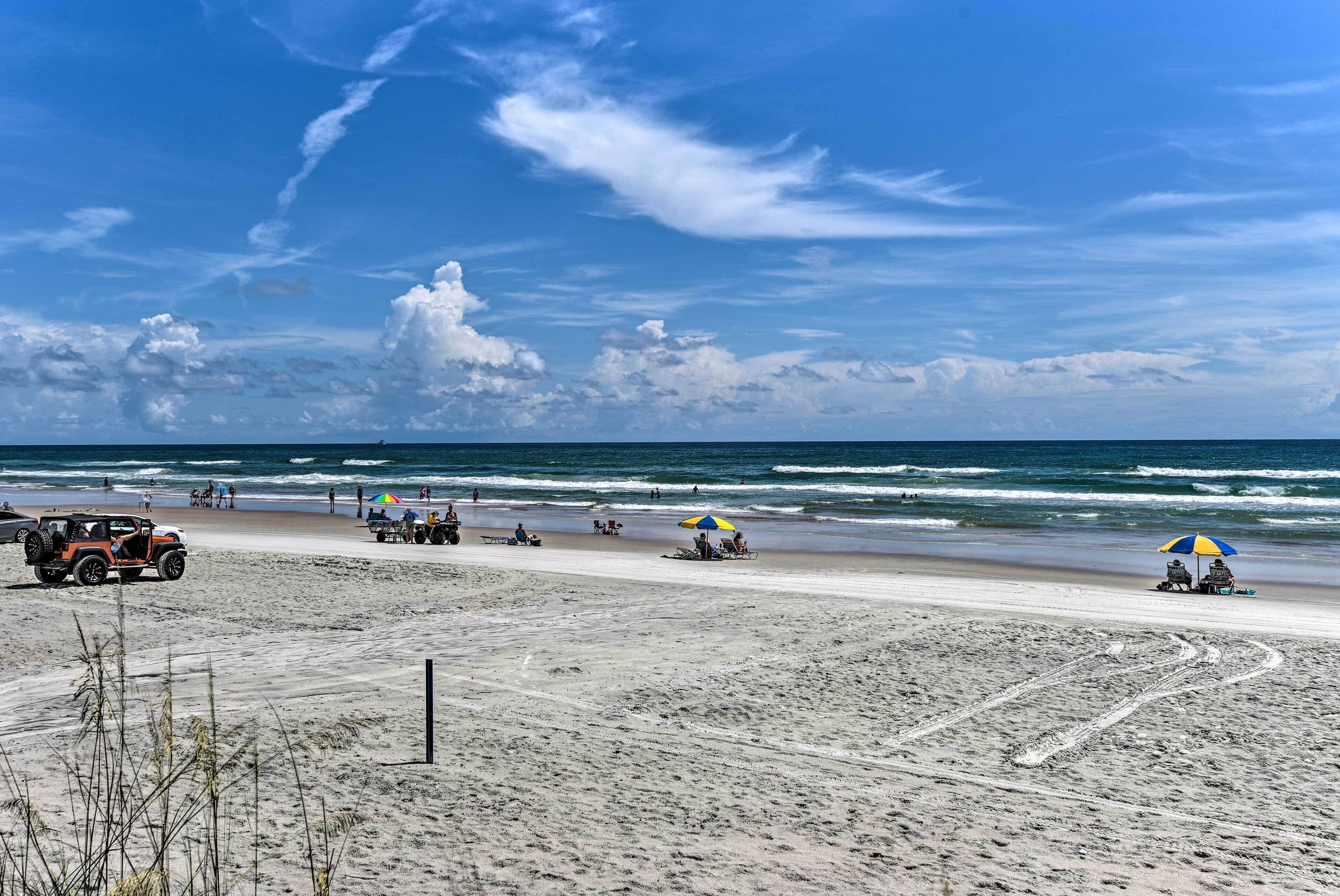 A beach with a Jeep, umbrellas, and people.