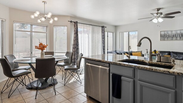 A modern kitchen with a central island, dining area with chairs, and a ceiling fan.