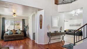 A spacious living room with hardwood flooring, a sofa set, a console table, and a staircase leading to an upper level.