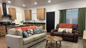 Un salon moderne avec un canapé, un fauteuil, une table basse et, au fond, un coin cuisine.
