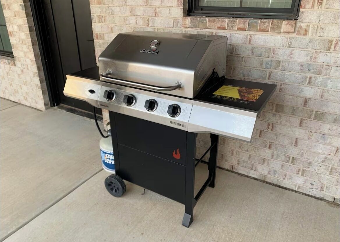 Una parrilla de gas portátil con cuatro quemadores, un estante lateral y una base negra con ruedas.