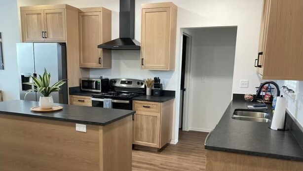 Une cuisine moderne avec des meubles en bois, un îlot central, des appareils électroménagers en acier inoxydable et un four à micro-ondes.
