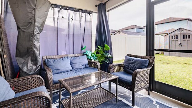 Un solárium con muebles de mimbre, una mesa de centro de vidrio y vistas al jardín trasero.