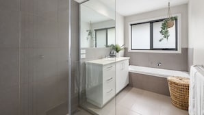 Uma casa de banho moderna com cabine de duche em vidro, toucador branco com lavatório e um espelho grande.