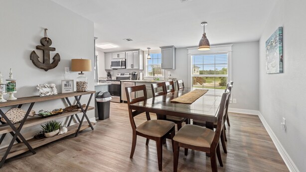 Una cocina moderna con armarios blancos, una zona de comedor con mesa de cristal y vistas al exterior.