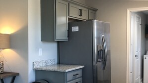 Una cocina con refrigerador de acero inoxidable, armarios grises, encimera de granito y un bote de basura.