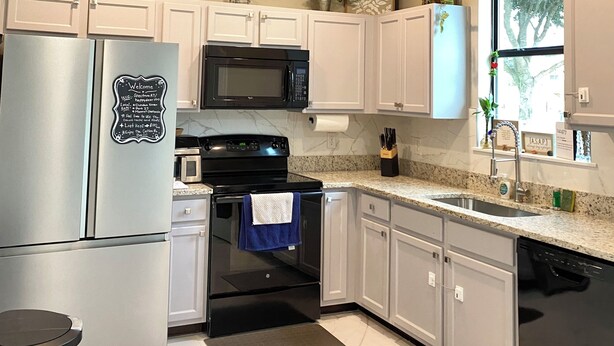 Una cocina moderna con gabinetes blancos, electrodomésticos de acero inoxidable, encimera de granito y ventana con vistas a árboles.