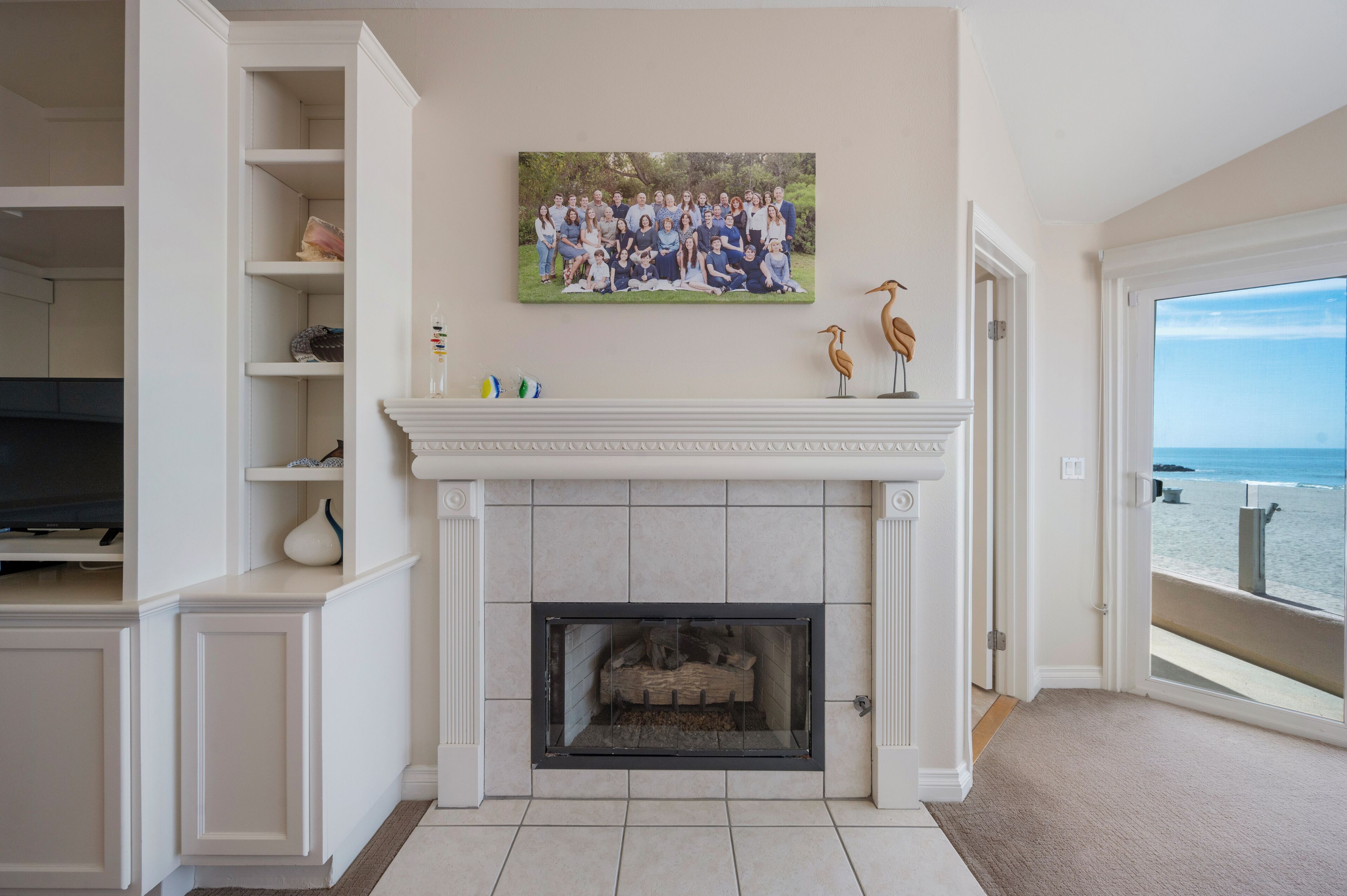 A living room with a fireplace, a mounted painting, and a view of the beach.
