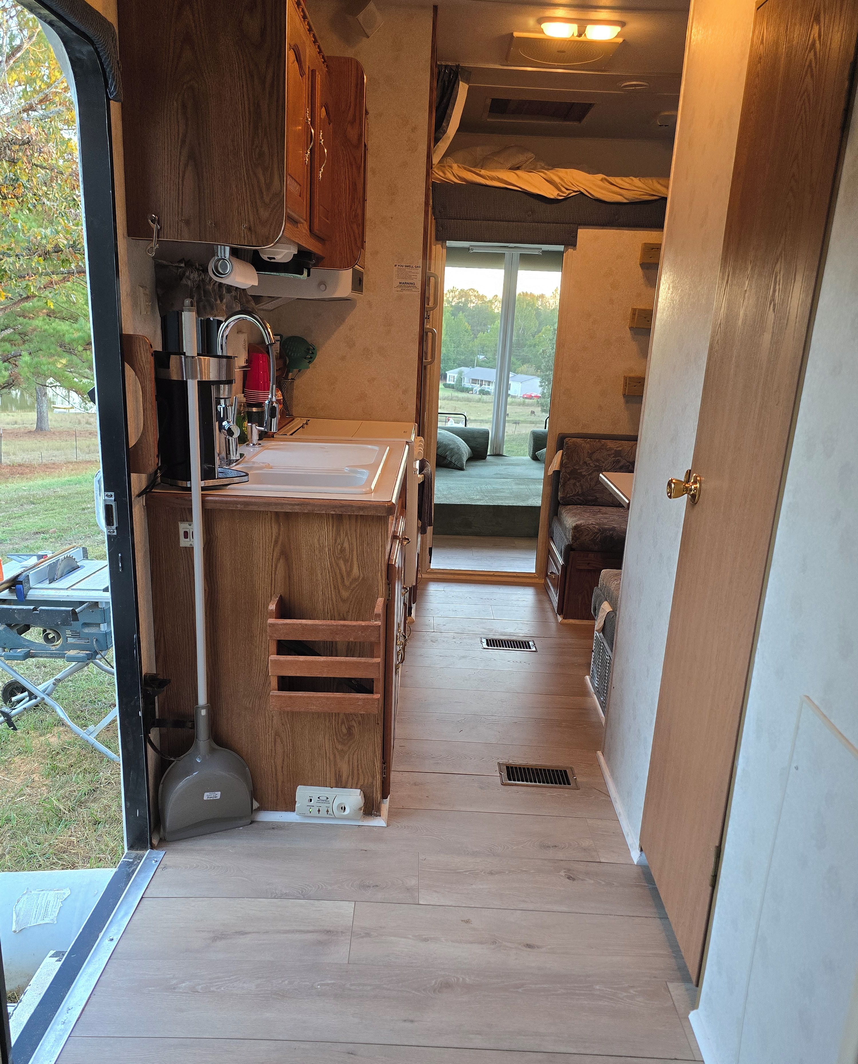 Une cuisine de taille réduite, avec des meubles de rangement en bois, un évier et un plan de travail. Une fenêtre offre une vue sur l’extérieur.