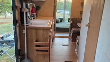 Une cuisine de taille réduite, avec des meubles de rangement en bois, un évier et un plan de travail. Une fenêtre offre une vue sur l’extérieur.