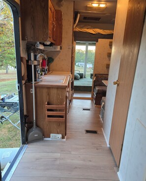 A compact kitchen with wooden cabinets, a sink, and a countertop. A window provides a view of the outdoors.
