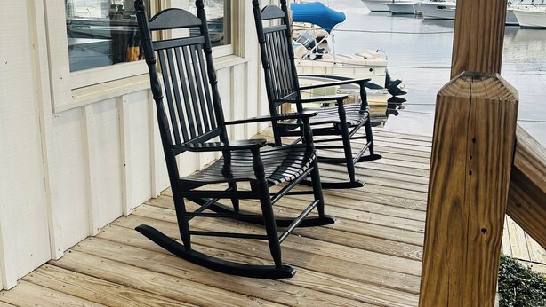Una terraza de madera con mecedoras, una cámara y vistas de barcos en el agua.