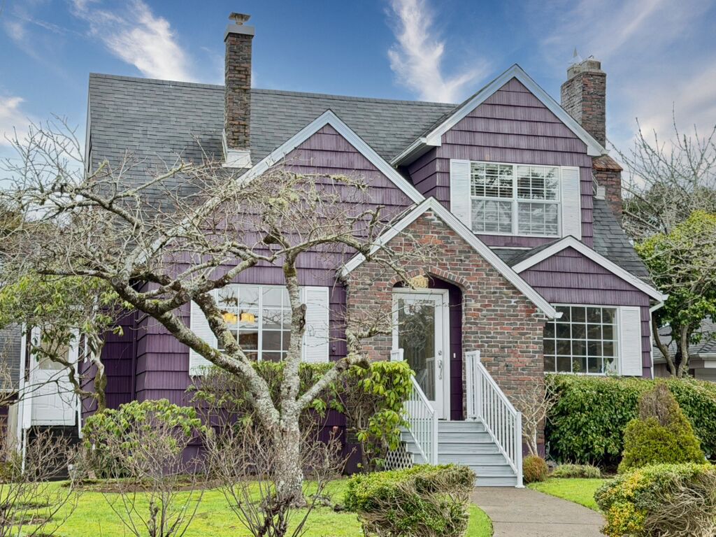 A two-story house with a brick chimney, a front porch, and a well-maintained lawn.