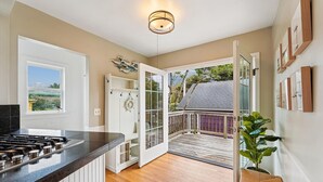 A kitchen with a black countertop, a white cabinet, and a wooden floor. There is a door leading to a balcony with a view of a house and a plant. - Historic Seaside Beach Home | Deck, Hot Tub, Games (Seaside)