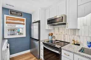 A modern kitchen with white cabinets, stainless steel appliances, and a blue accent wall.