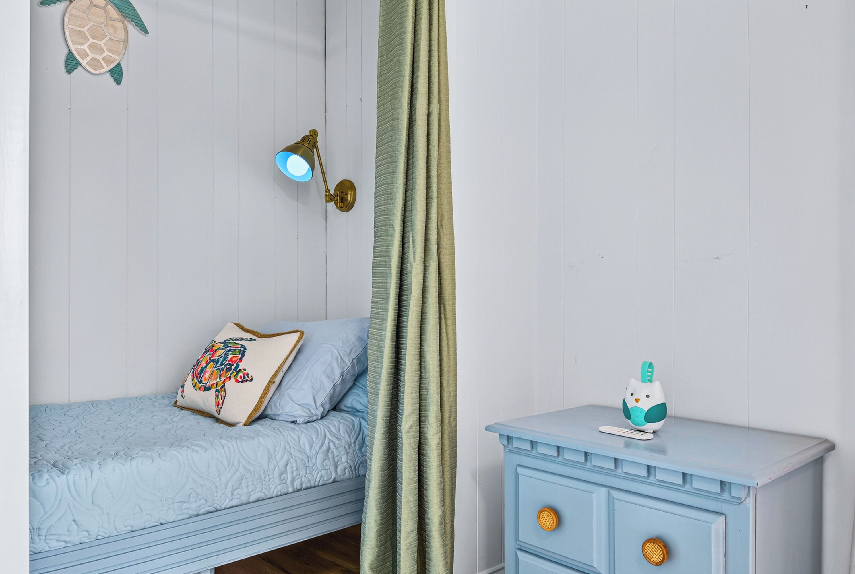 A bedroom with a bed, a nightstand, a wall-mounted lamp, and a curtain.