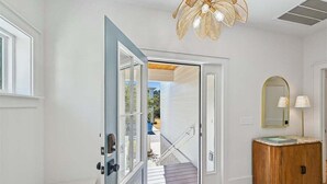 A modern interior with a wooden floor, a white door leading to an outdoor area, a ceiling fan, and a wooden cabinet with a mirror. - Now Offering up to 25% OFF Fall 2026, New in 2026 , Steps to Beach, Pool, Free Golf, Dogs OK (Hilton Head Island)