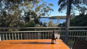 A wooden table with a bottle of wine and two glasses on a balcony overlooking a lake. - Culburra Beach Lake House (Culburra Beach)