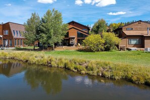 A modern house with a large deck, a pond, and a well-maintained lawn.