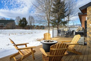 A wooden deck with outdoor seating, a fire pit, and a grill area.