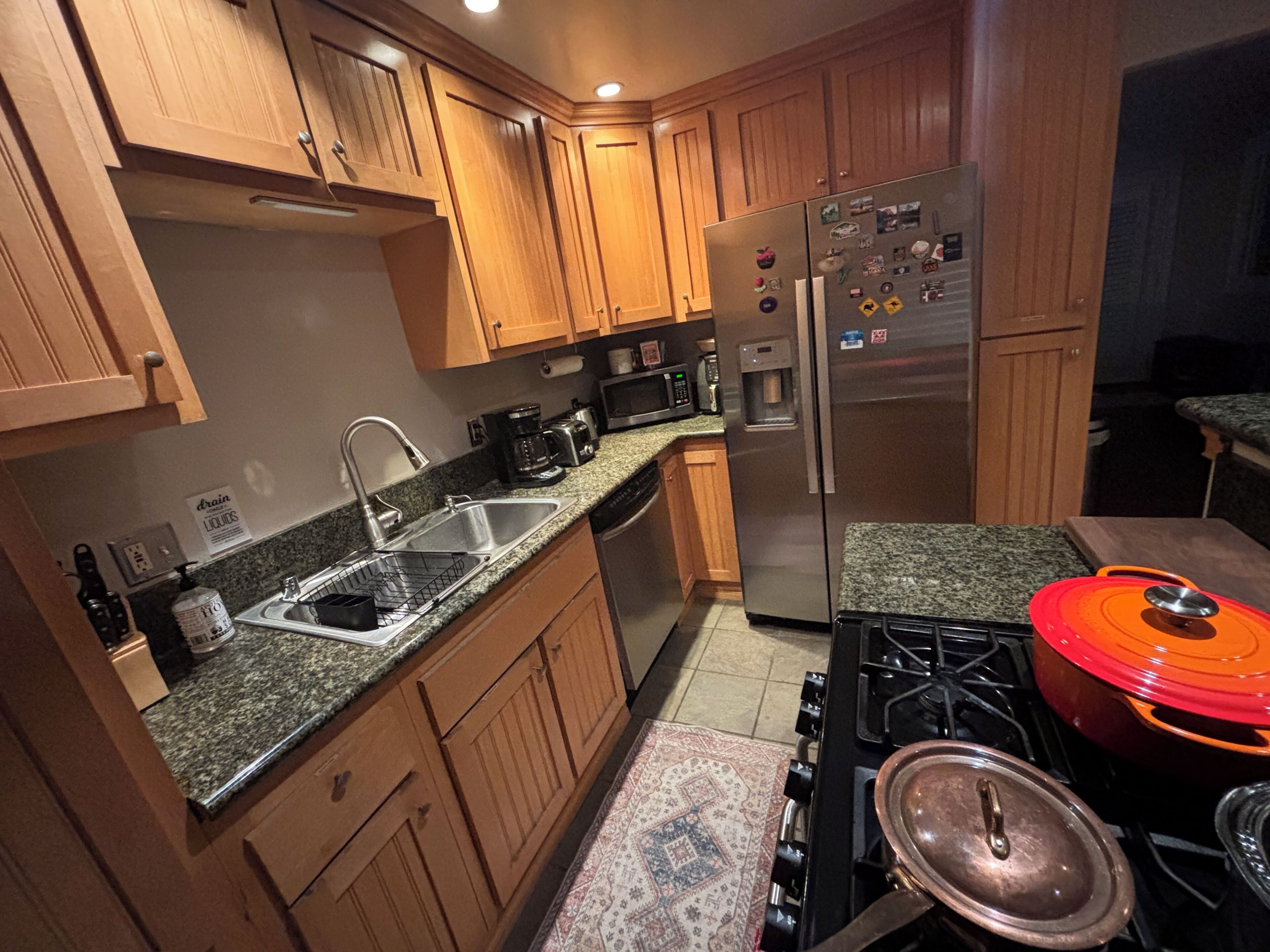 A kitchen with wooden cabinets, a stainless steel refrigerator, a sink, a stove, and a microwave.