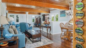 A spacious living room with a wooden ceiling, a dining area with a wooden table and chairs, and a kitchen area visible through an open door. - The Lazy Lake House on Center Hill (Sparta)