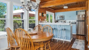 A wooden dining table with chairs, a chandelier, and a kitchen with a refrigerator and microwave. - The Lazy Lake House on Center Hill (Sparta)